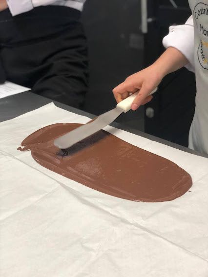 Chocolate sendo trabalhado com uma espátula durante uma aula de confeitaria.